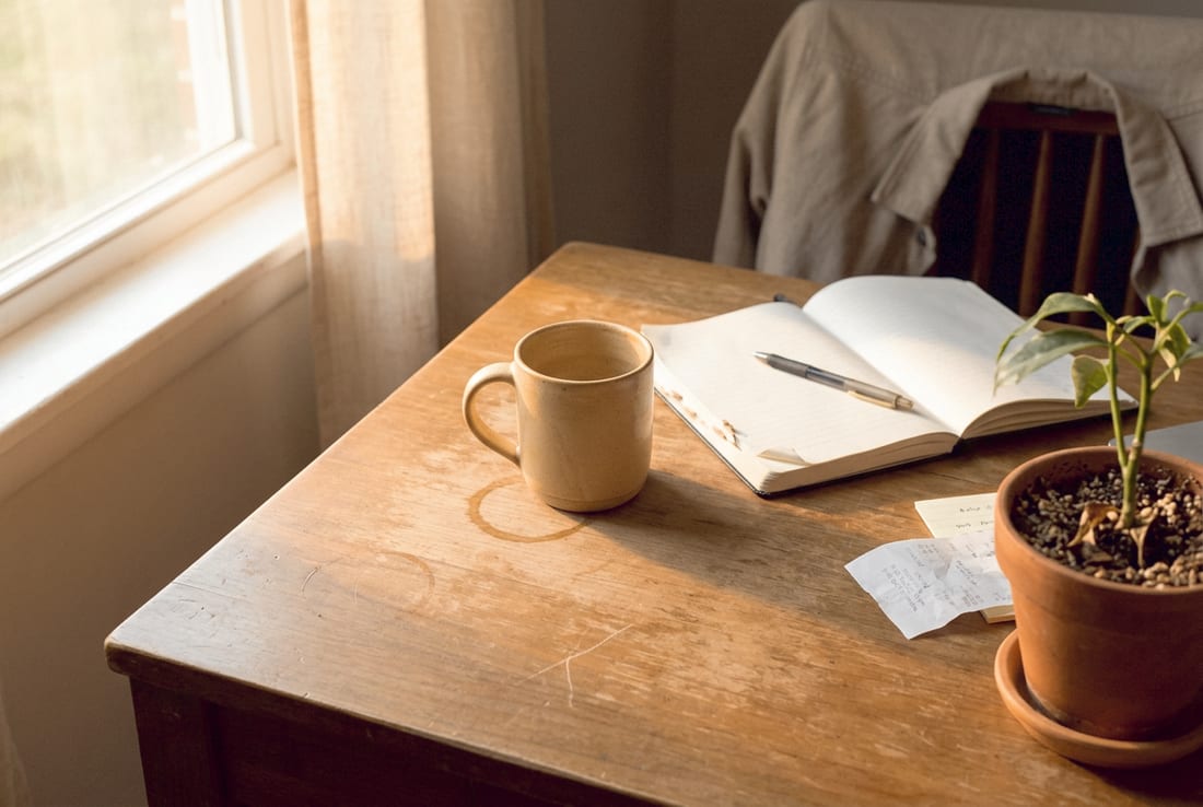 Warmer Schreibtisch mit Notizbuch und Kaffee – unkompliziert Kontakt aufnehmen.