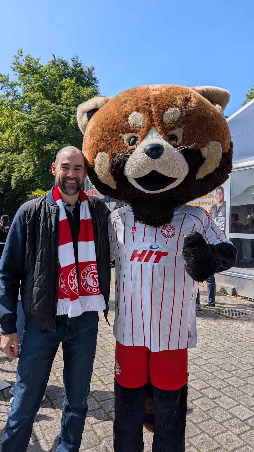 Marco, Inhaber von KEIN HECKMECK, mit Fortuna-Köln-Schal und Maskottchen Fred.